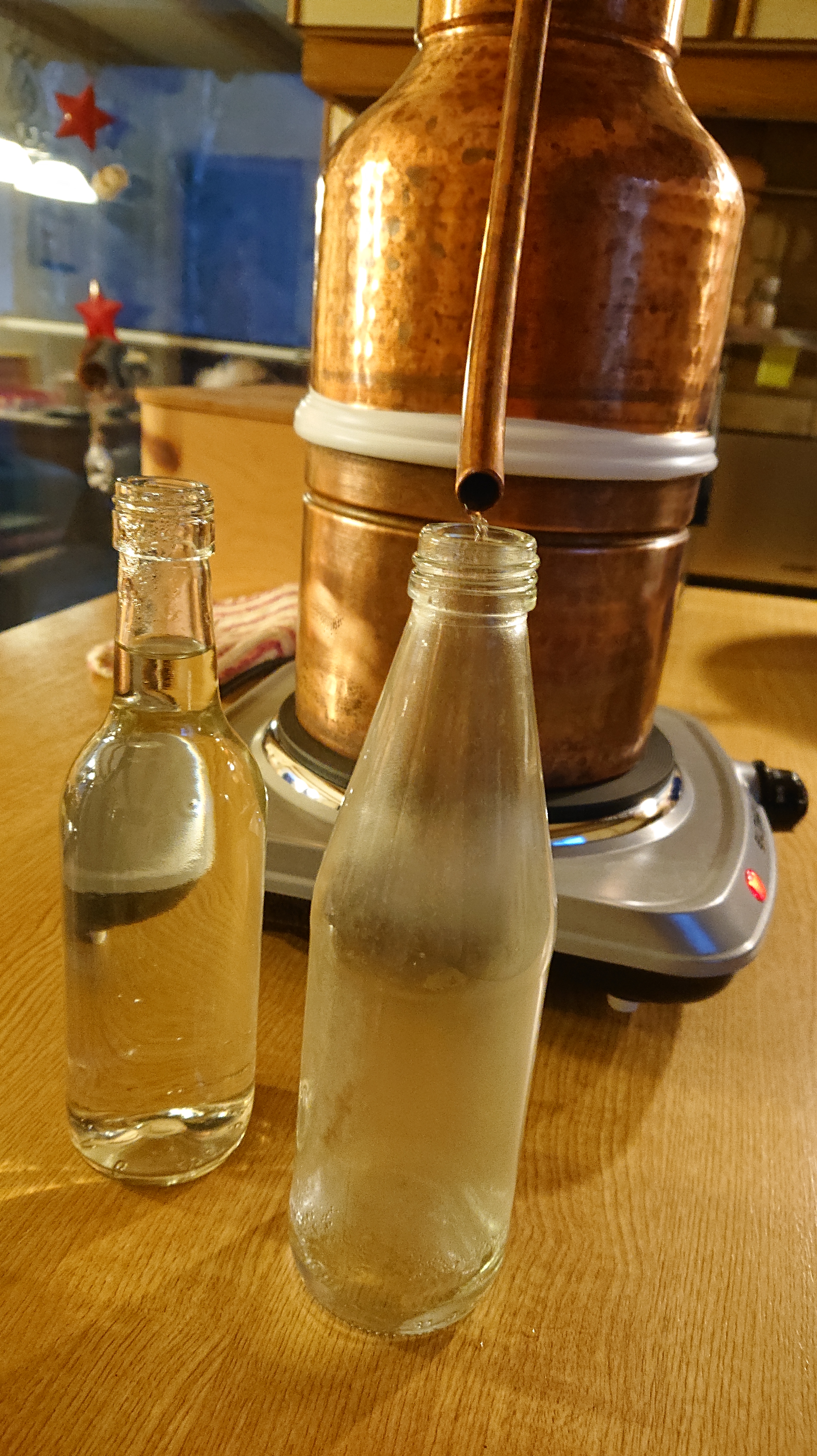 zwei Flaschen mit Hydrolat stehen vor einer Destille.